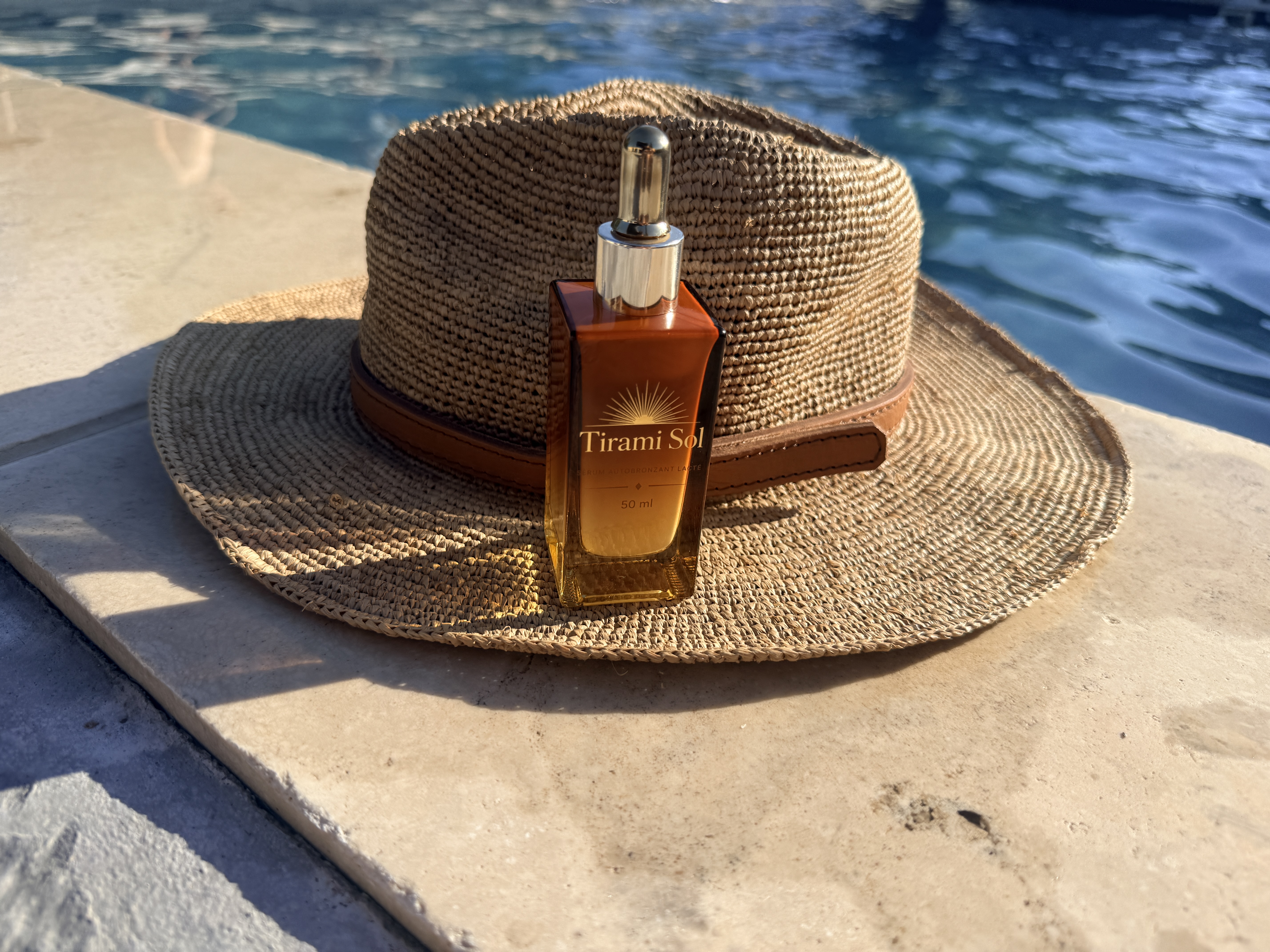 Photo du flacon TiraMiSol 50 ml sur un chapeau de paille, au bord de la piscine